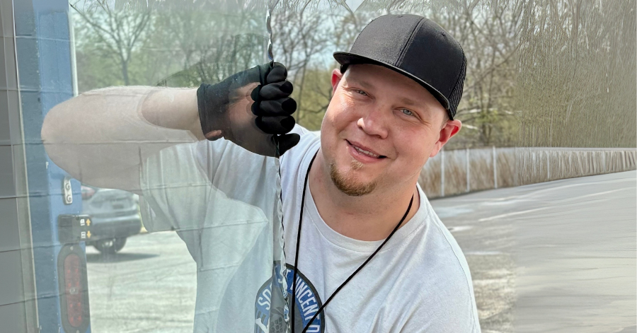 Man holding plastic screen wearing hat, smiling