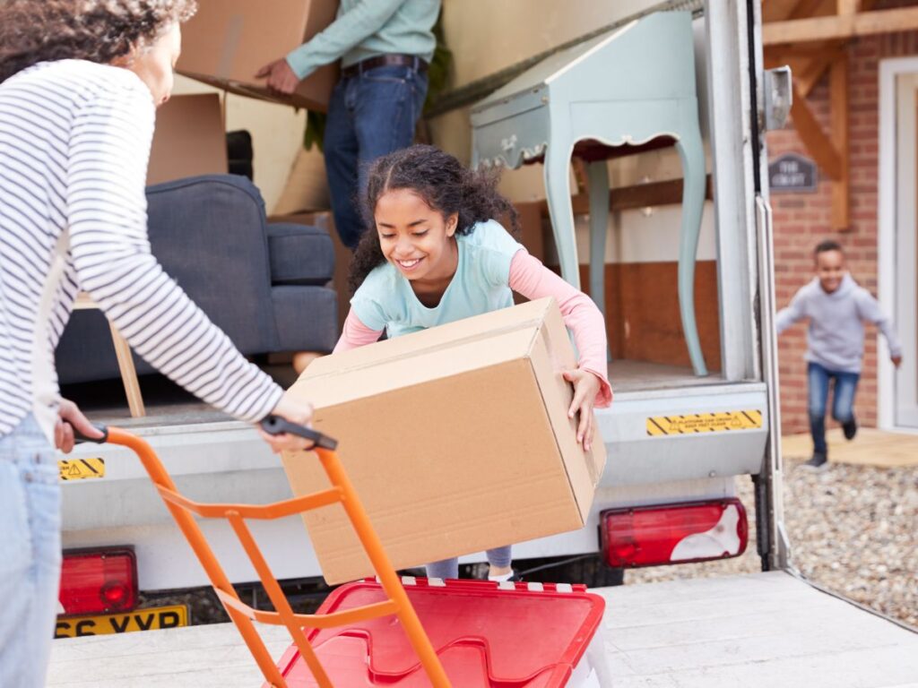 Child setting box down on dolly with moving truck in background