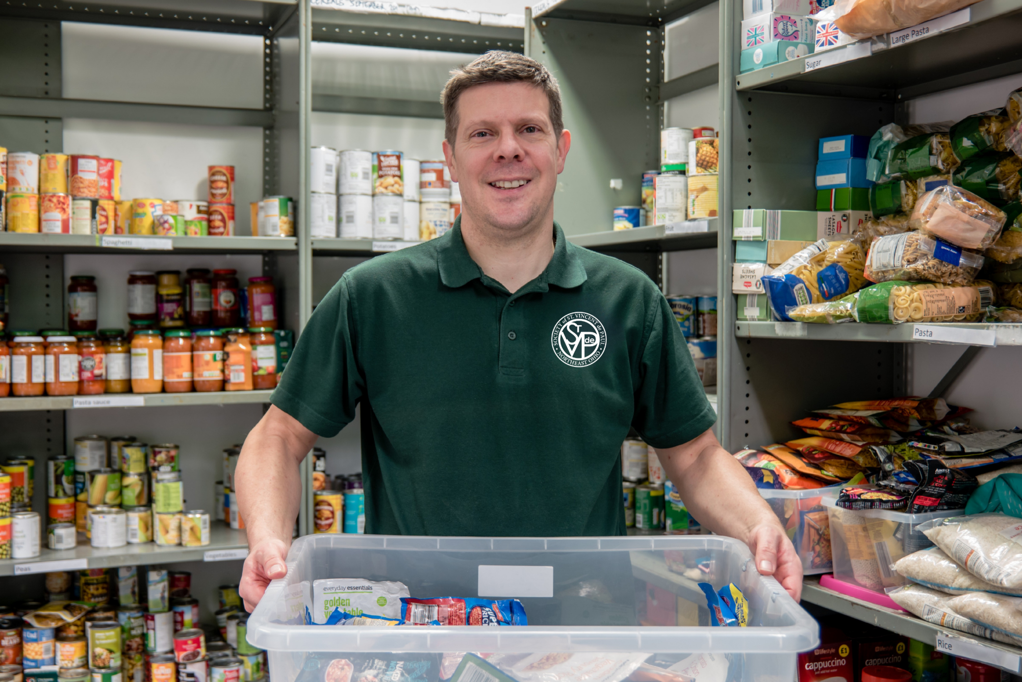 Man wearing SVDP green polo in food pantry holding big plastic tub