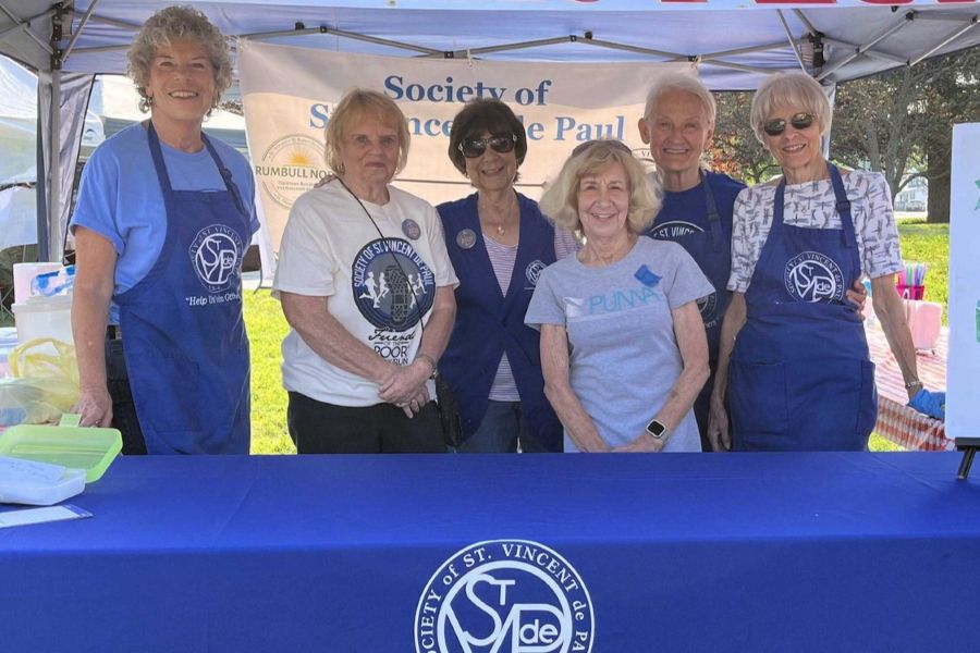 Group of older people wearing SVDP attire standing behind table, smiling