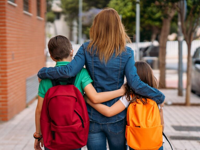 Mom with arms around children with bookbags