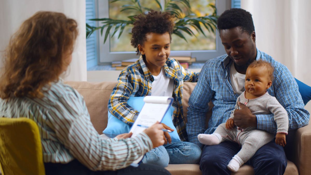 Family of father and 2 children sitting on couch talking with woman
