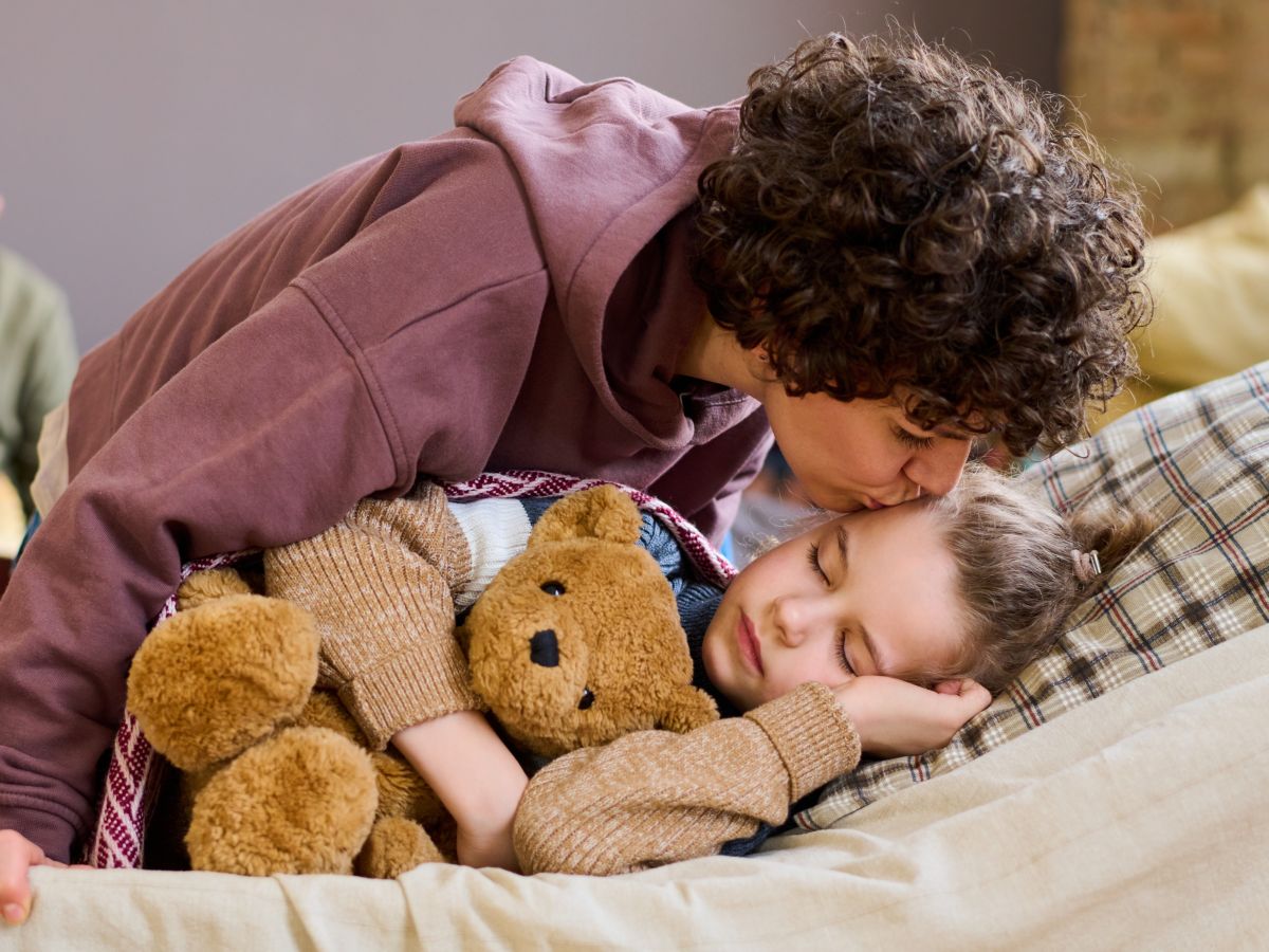 Mom kissing sleeping child holding teddy bear